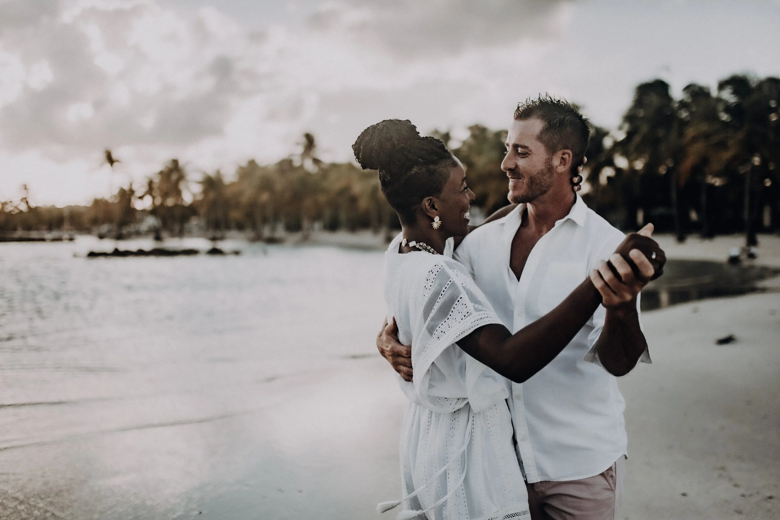 Photographie de couple à Sainte-Anne – C & S 07 Couple enlacé et souriant sur la plage de Sainte-Anne, avec les palmiers en arrière-plan