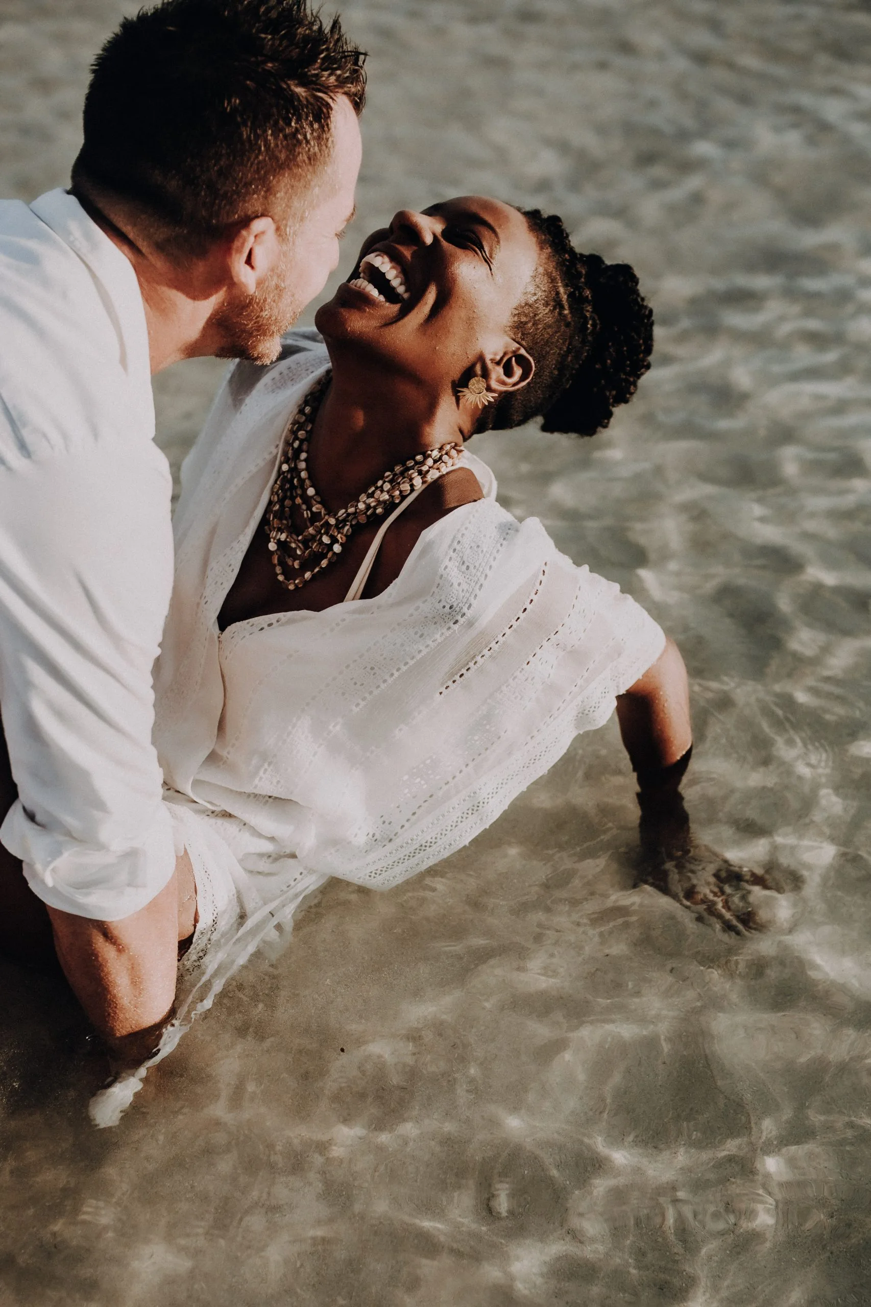 Séance couple au bord de l'eau – C & S 04 Femme en chemise blanche dans les bras de son compagnon au bord de l'eau à Sainte-Anne