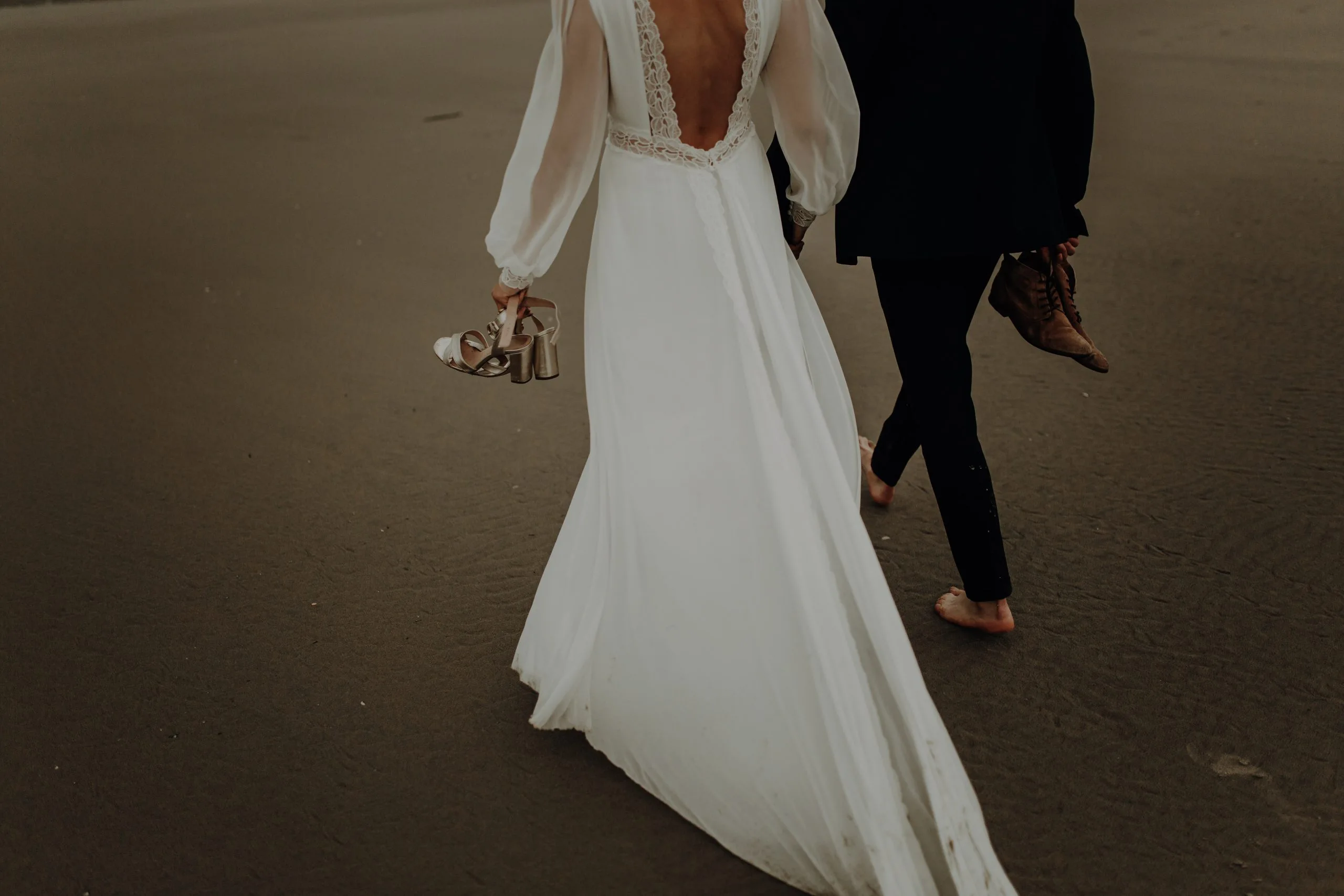 Blanche et Lucas marchent pieds nus sur le sable du Touquet, leurs chaussures à la main, la traîne de la robe de mariée effleurant le sol.