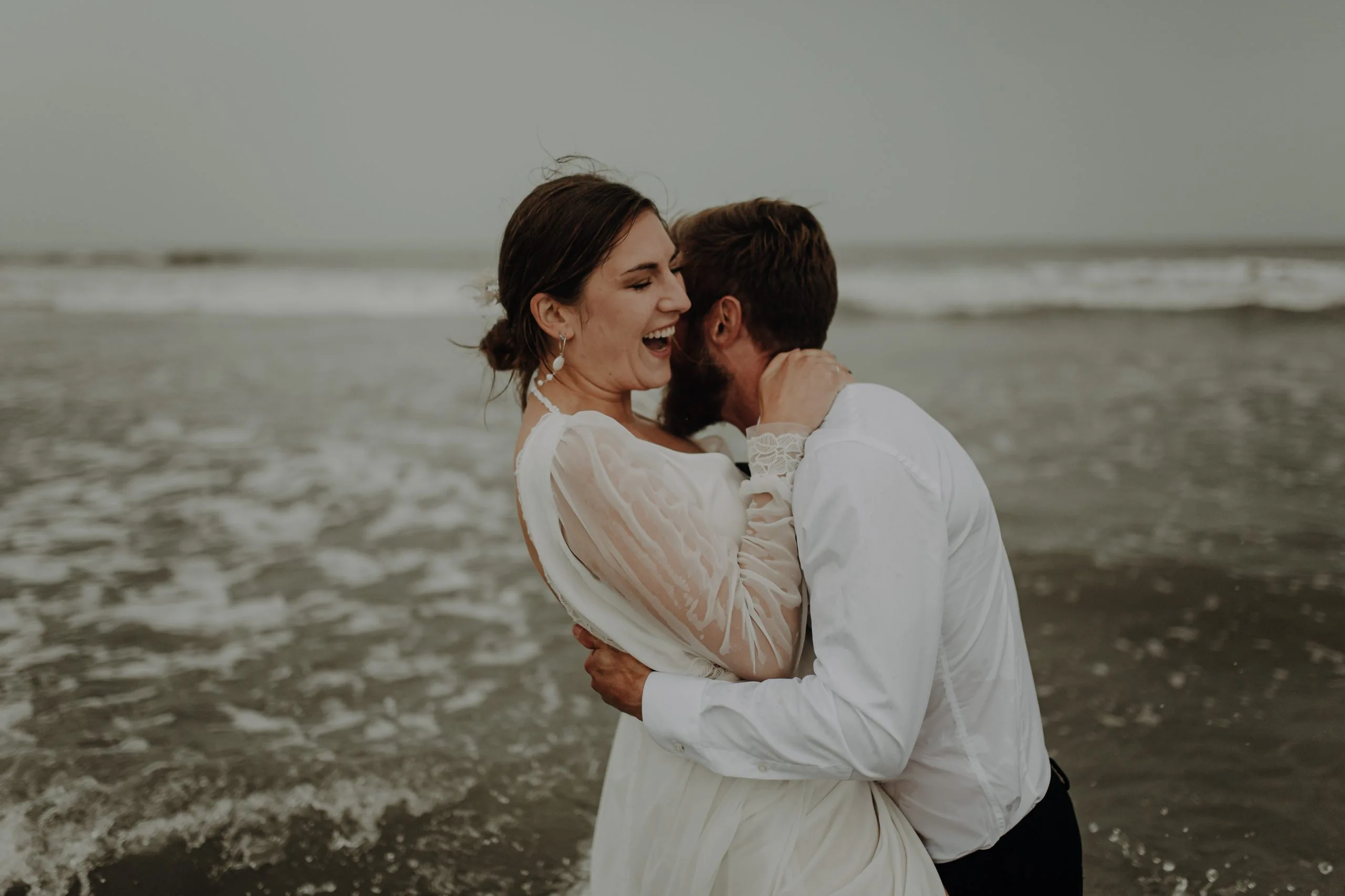 Blanche rit dans les bras de Lucas sur la plage du Touquet lors de leur séance photo après-mariage.