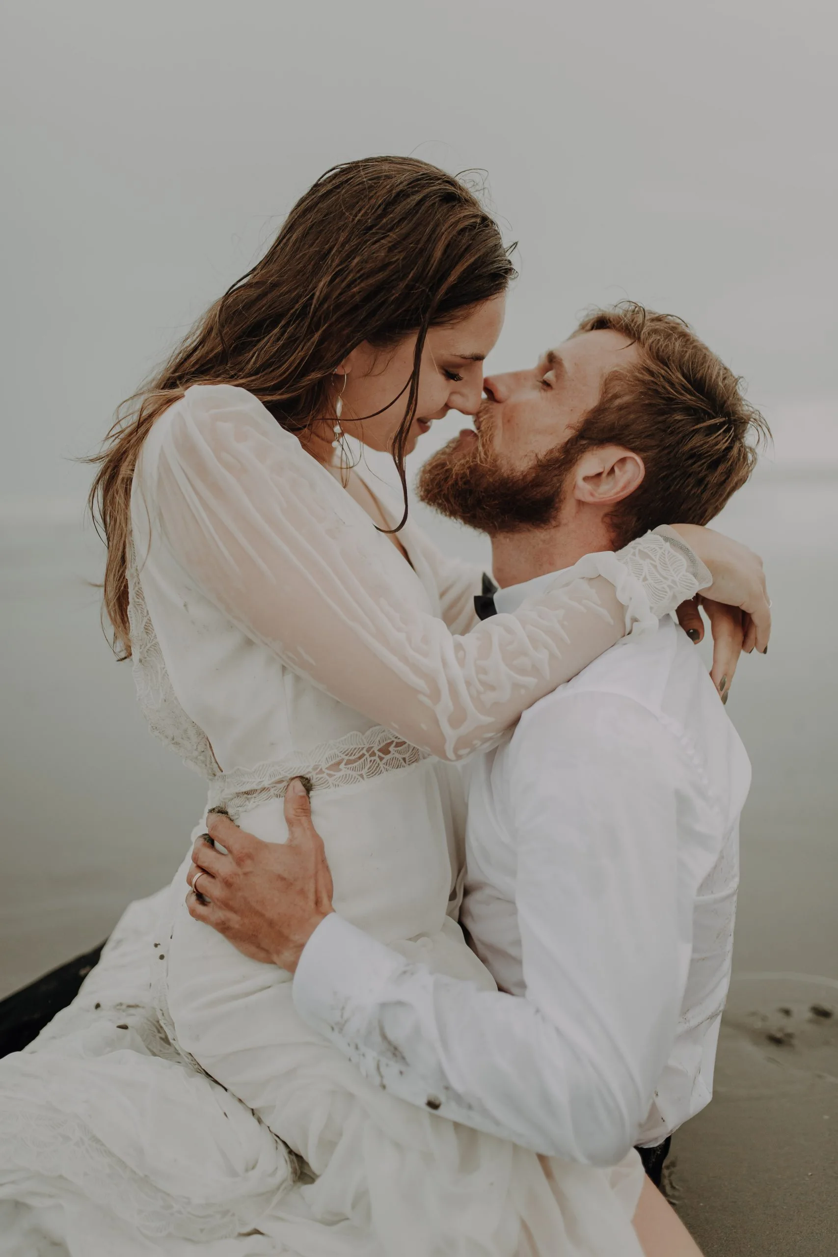 Blanche et Lucas s'embrassent tendrement sur la plage, vêtus de leurs tenues de mariage.