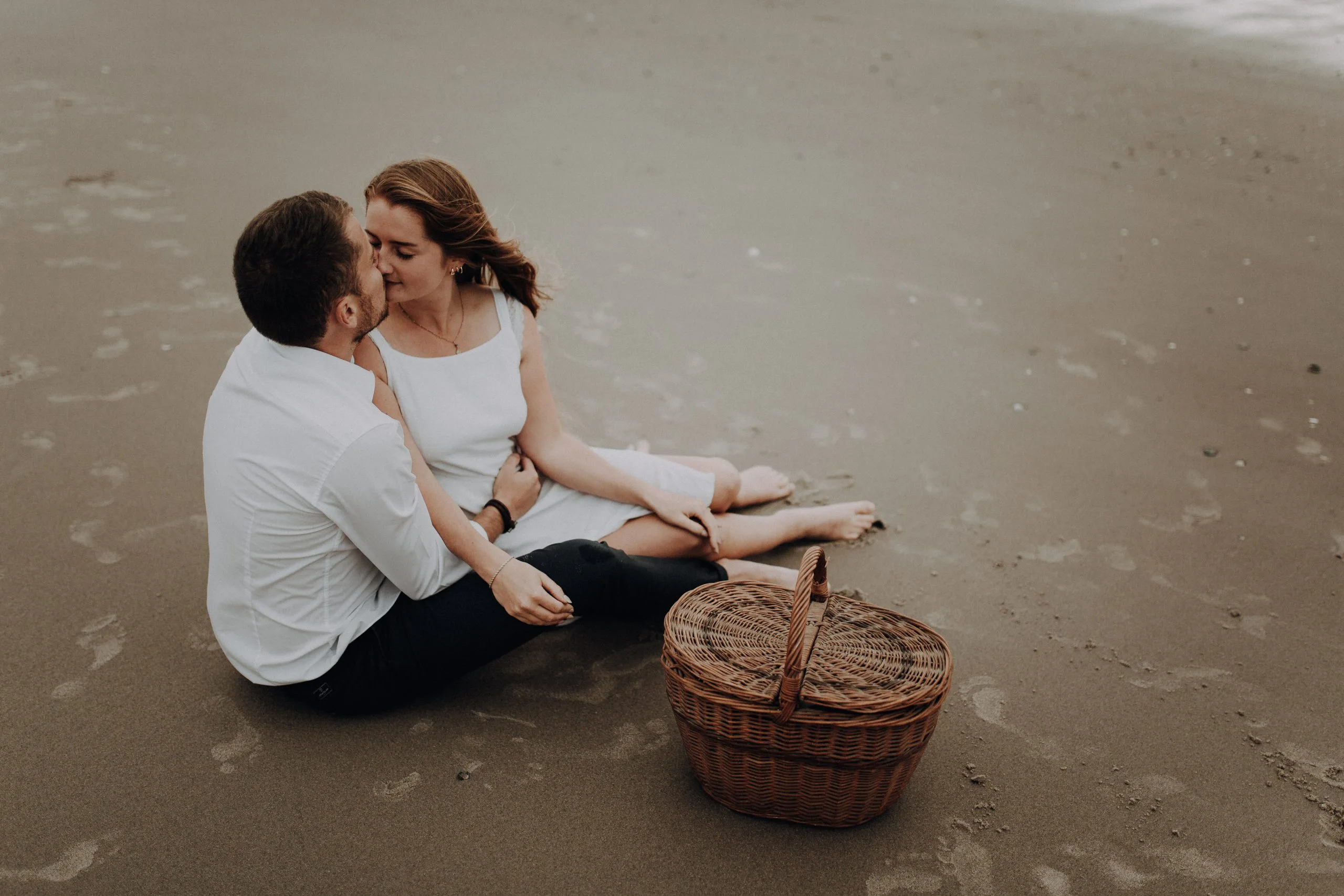 Couple assis sur une couverture sur le sable, la femme sur les genoux de son compagnon