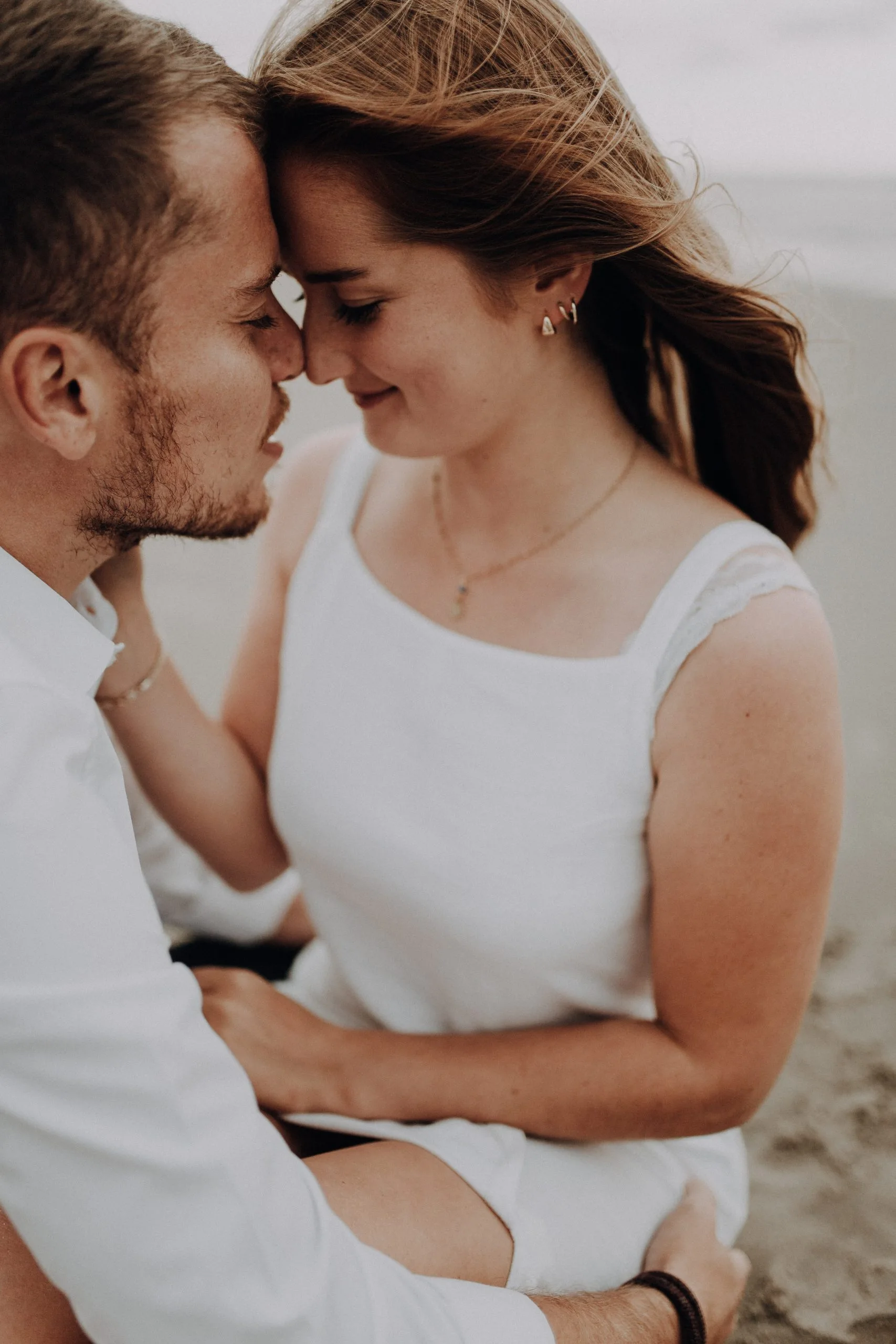 Couple front contre front sur la plage, la femme portant une robe blanche