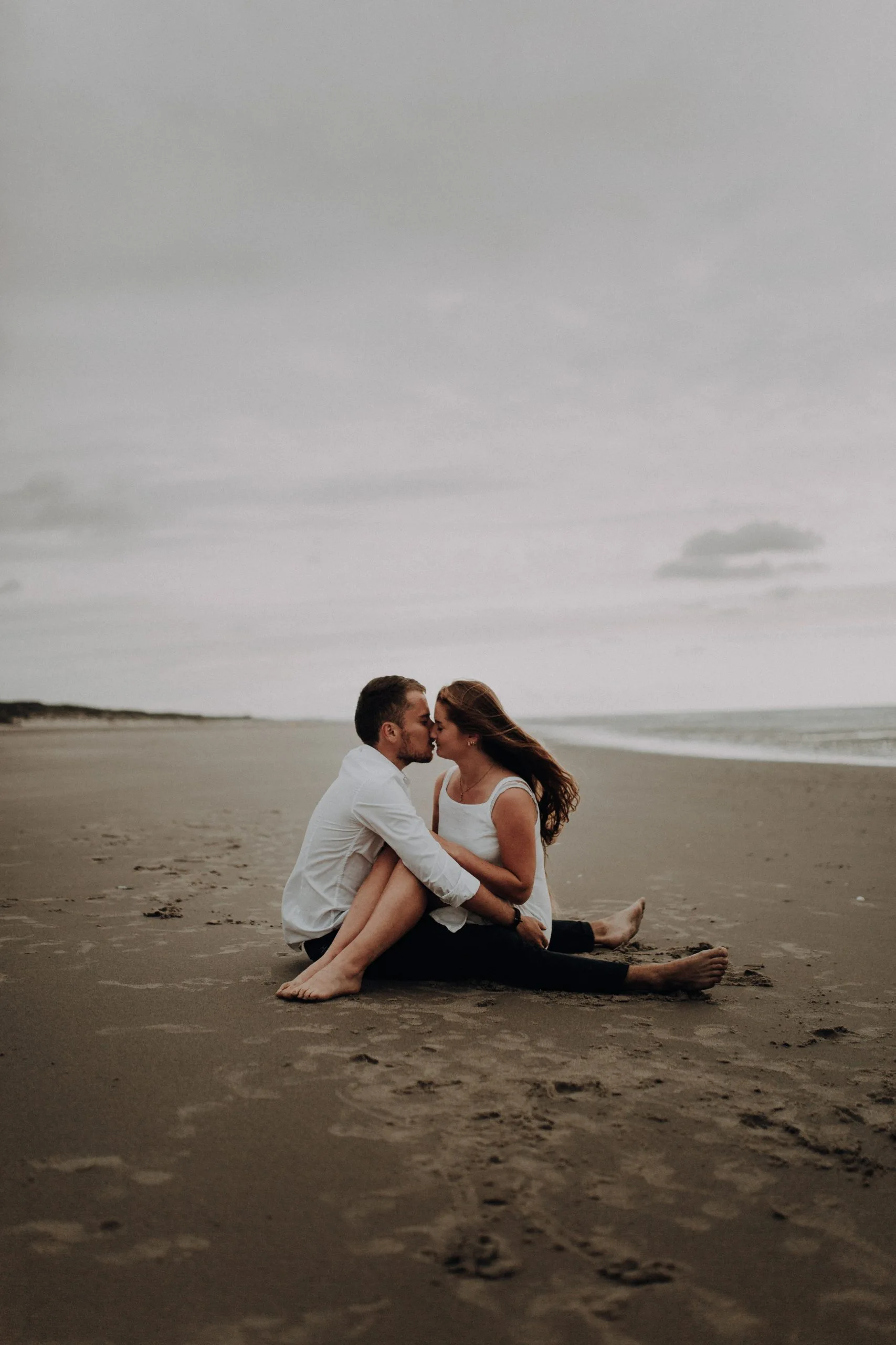 Couple se rapprochant pour s'embrasser sur une plage immense sous un ciel gris