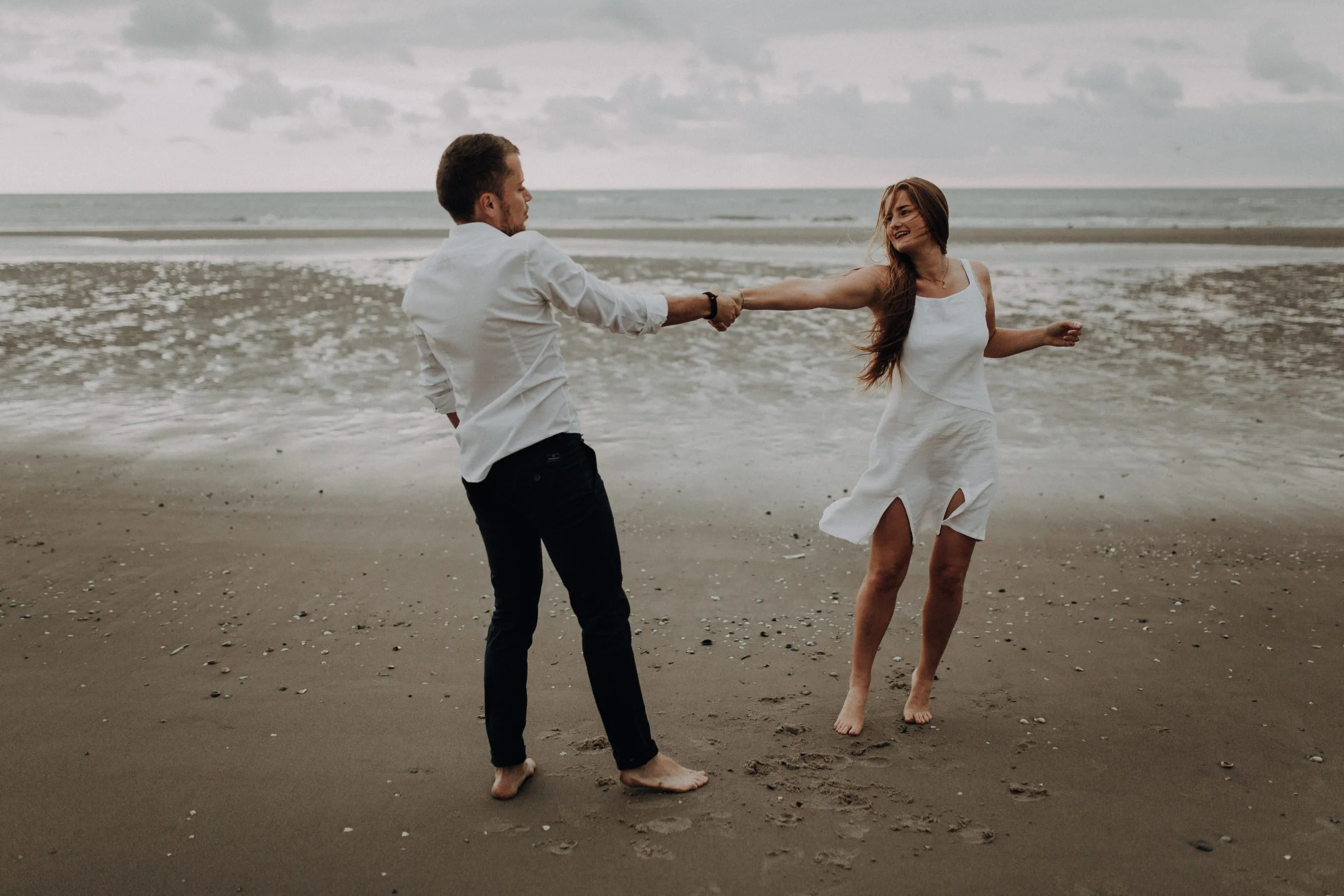 Couple se tenant par la main et jouant sur le sable humide face à la mer