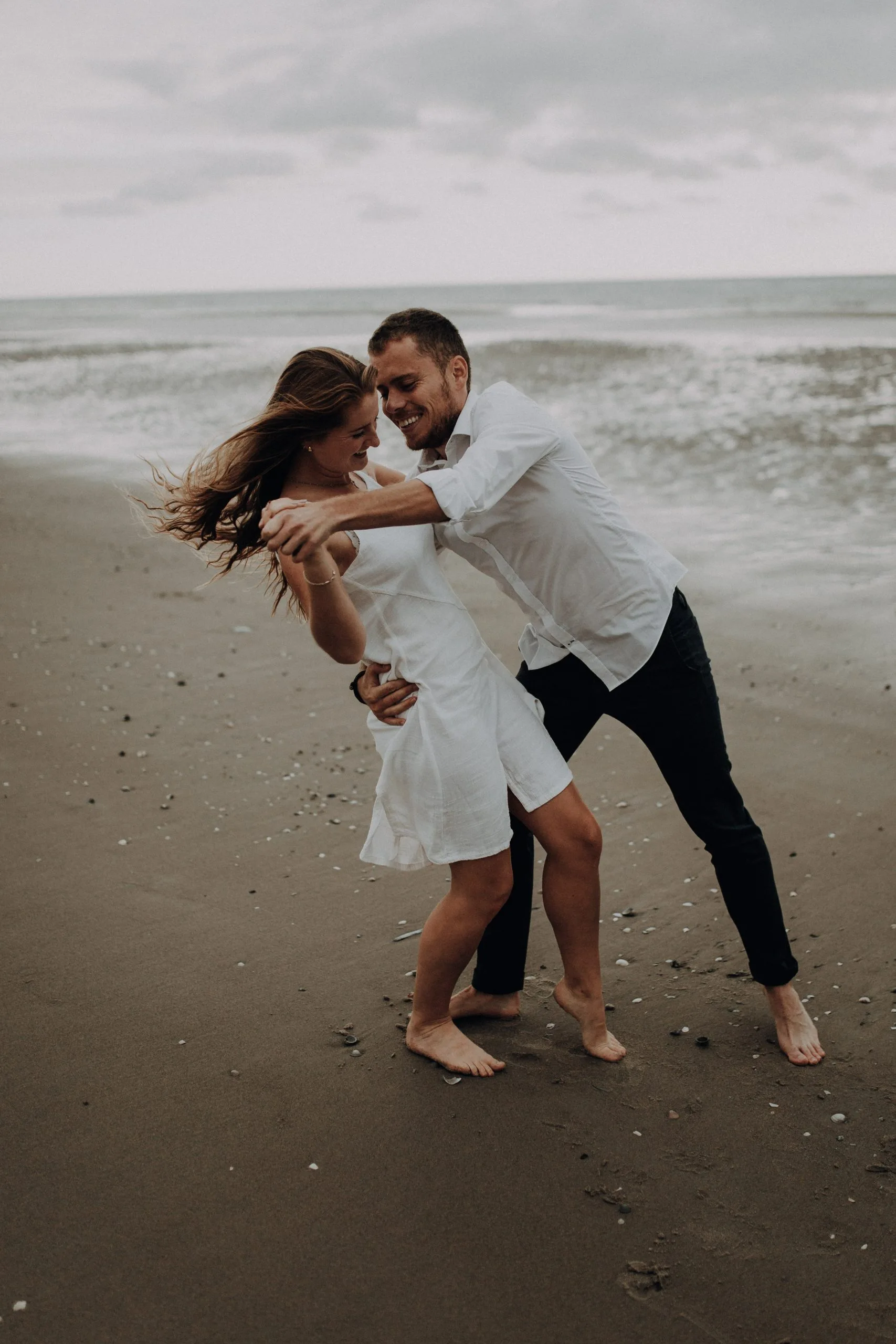 Couple en mouvement sur la plage, l'homme tenant sa compagne dans ses bras près des vagues
