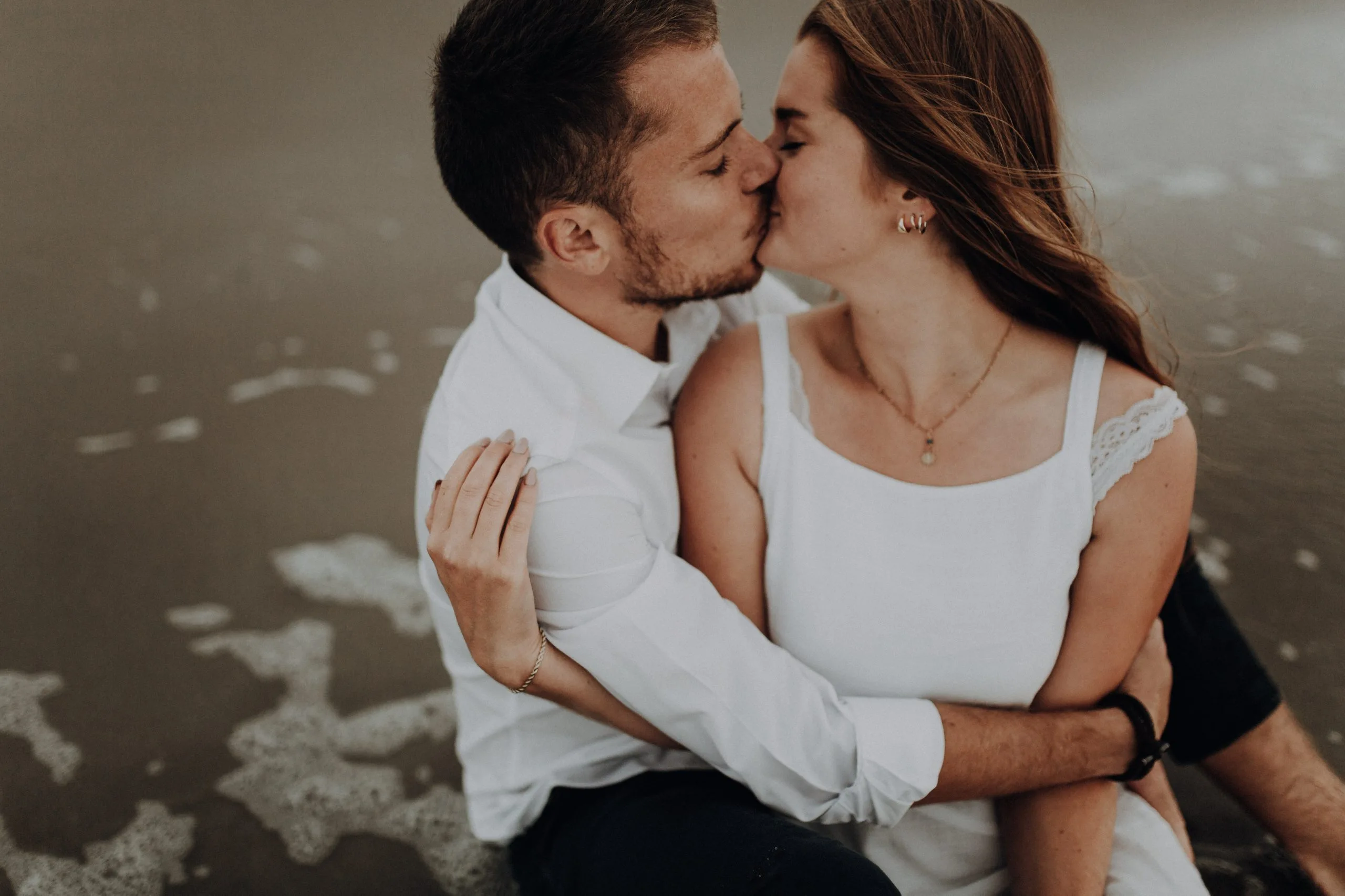 Couple échangeant un baiser sur la plage, vêtus de blanc, photographié en plan rapproché