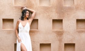 Portrait d'une mariée en robe blanche devant un mur ocre aux niches carrées à Marrakech