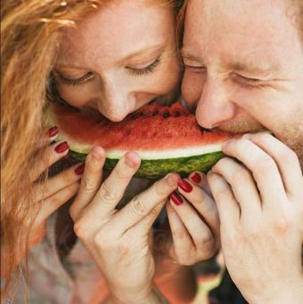 Couple souriant en croquant ensemble dans une grande tranche de pastèque.
