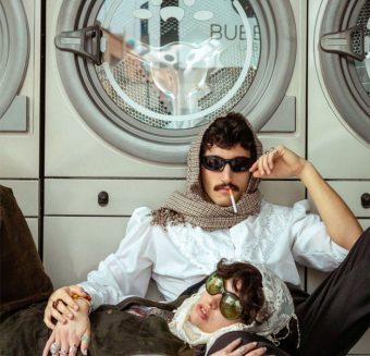 Homme portant des lunettes de soleil, assis devant les machines à laver d'une laverie.