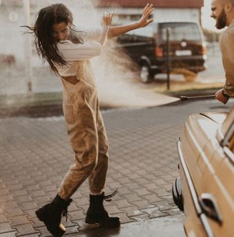 Femme jouant avec de l'eau près d'une voiture, lors d'une scène estivale en extérieur.
