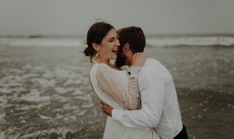 Blanche rit dans les bras de Lucas sur la plage du Touquet lors de leur séance photo après-mariage.