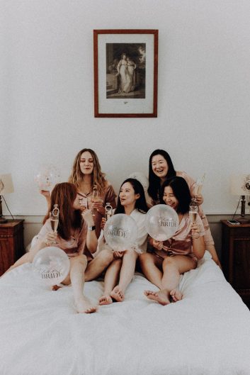 La mariée assise sur le lit en compagnie des ses témoins avec des ballons et des coupes de champagnes