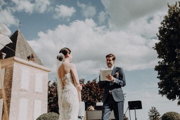 Les mariés debout en extérieur pendant la cérémonie sous un ciel bleu nuageux au Château Lacoste.