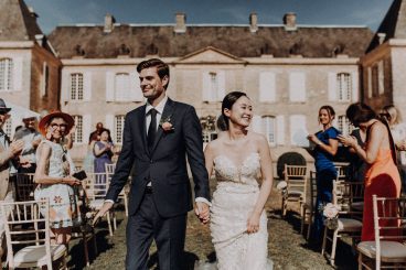 Les mariés marchant devant le château entourés de leurs invités après la cérémonie de mariage.