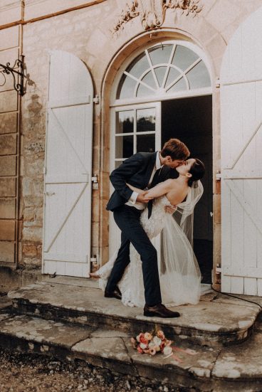 Marié portant son épouse devant une grande fenêtre du château pendant leur séance photo de mariage.