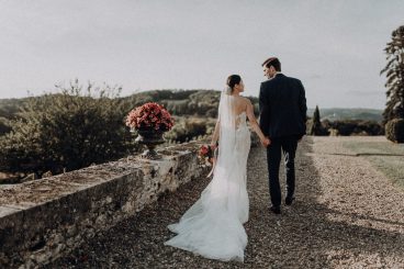 Couple de mariés debout sur une terrasse du château face aux jardins et au paysage environnant.