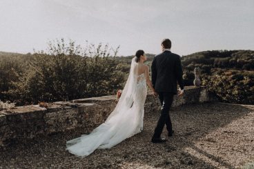 Les mariés vus de dos marchant sur une terrasse avec les paysages du Château Lacoste en arrière-plan.