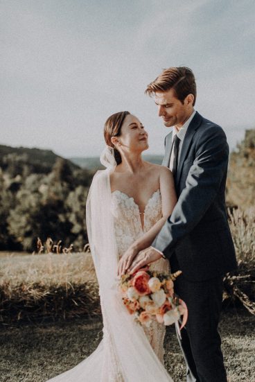 Portrait rapproché des jeunes mariés enlacés tenant le bouquet de la mariée dans la lumière naturelle du domaine.