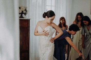 Plusieurs femmes aidant la mariée à ajuster sa robe blanche pendant les préparatifs dans une chambre du château.