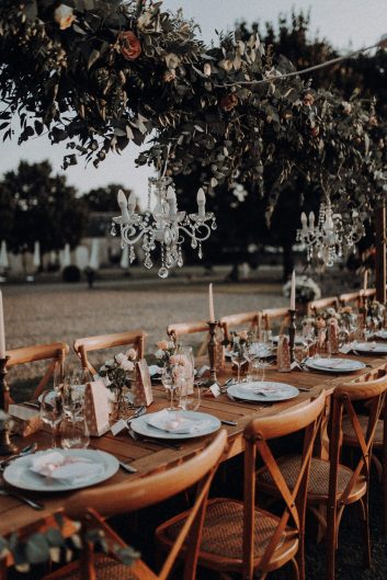 Table de mariage décorée en extérieur sous les arbres avec des chandeliers et une décoration élégante.