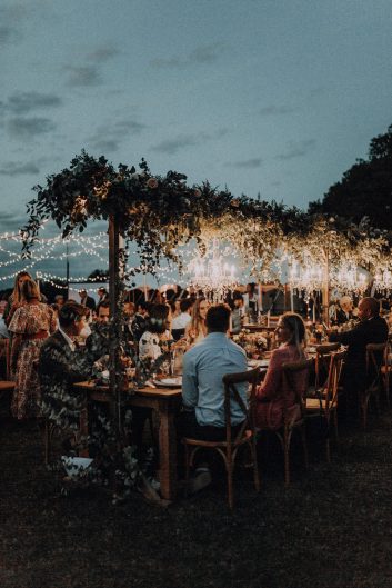 Vue nocturne des tables de réception décorées et illuminées pendant un mariage au château.