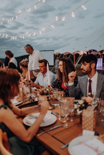 Vue d'ensemble du dîner de mariage avec les invités attablés sous des guirlandes lumineuses.