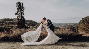 Couple de mariés s'embrassant dans un paysage naturel avec le long voile de la mariée déployé derrière elle.