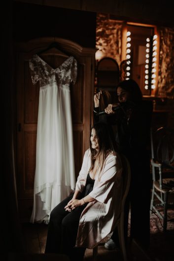 Château des Girards - La robe de mariée suspendue Robe de mariée blanche suspendue dans une pièce ancienne avec un éclairage chaleureux.