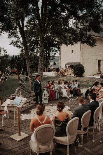 Château des Girards - Cérémonie intime sous les arbres Cérémonie de mariage en extérieur avec des invités réunis sous les arbres près d'un bâtiment en pierre.