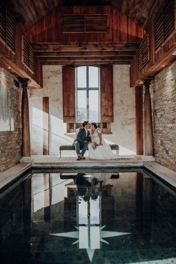 Château des Girards - Les mariés sous la grande porte Couple de mariés assis dans l'encadrement d'une grande porte en bois à l'intérieur d'un bâtiment ancien.