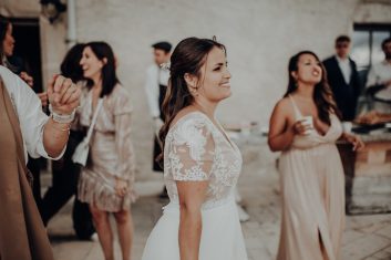 Château des Girards - Sourires autour de la mariée Mariée souriante en robe de dentelle entourée de plusieurs invitées dans une salle de réception.