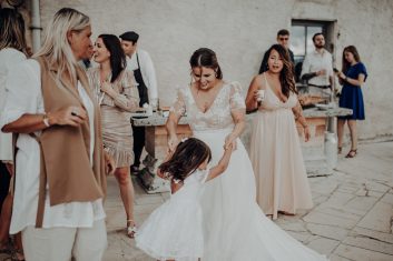 Château des Girards - Complicité entre les invitées Mariée en robe blanche entourée de plusieurs femmes élégamment habillées dans une pièce lumineuse.dansant une une petite fille
